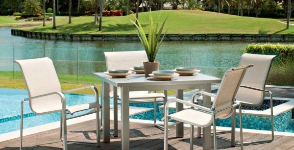 luxury patio including cream colored outdoor chairs and a light colored square breakfast table overlooking the pool