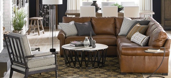 luxury living room featuring brown leather sofa with pillows, a brown diamond patterned area rug, round table, and off white patterned chair