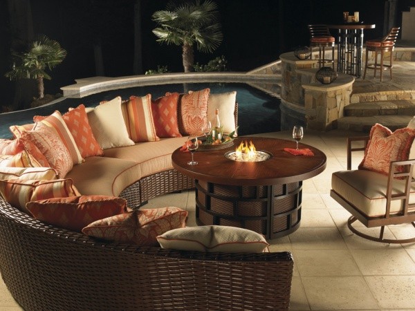 luxury patio including round wooden table, wicker wraparound outdoor sofa loaded with orange and cream pillows, with brown outdoor chair